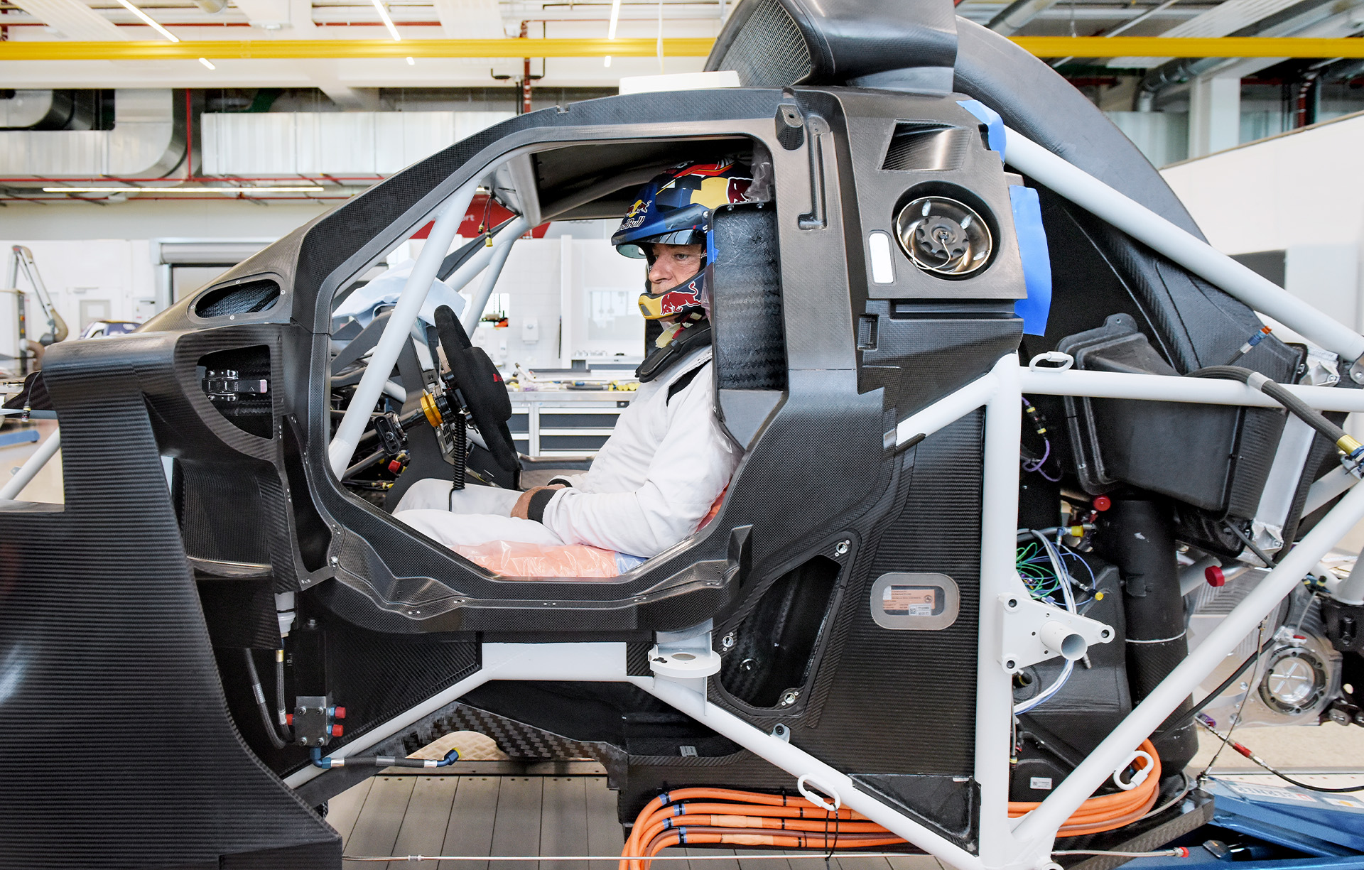  Carlos Sainz, jeden z kierowców Rajdu Dakar należący do Audi Sport, w klatce samochodu rajdowego przy montażu siedzenia. Siedzi za kierownicą na pomarańczowej piankowej poduszce.