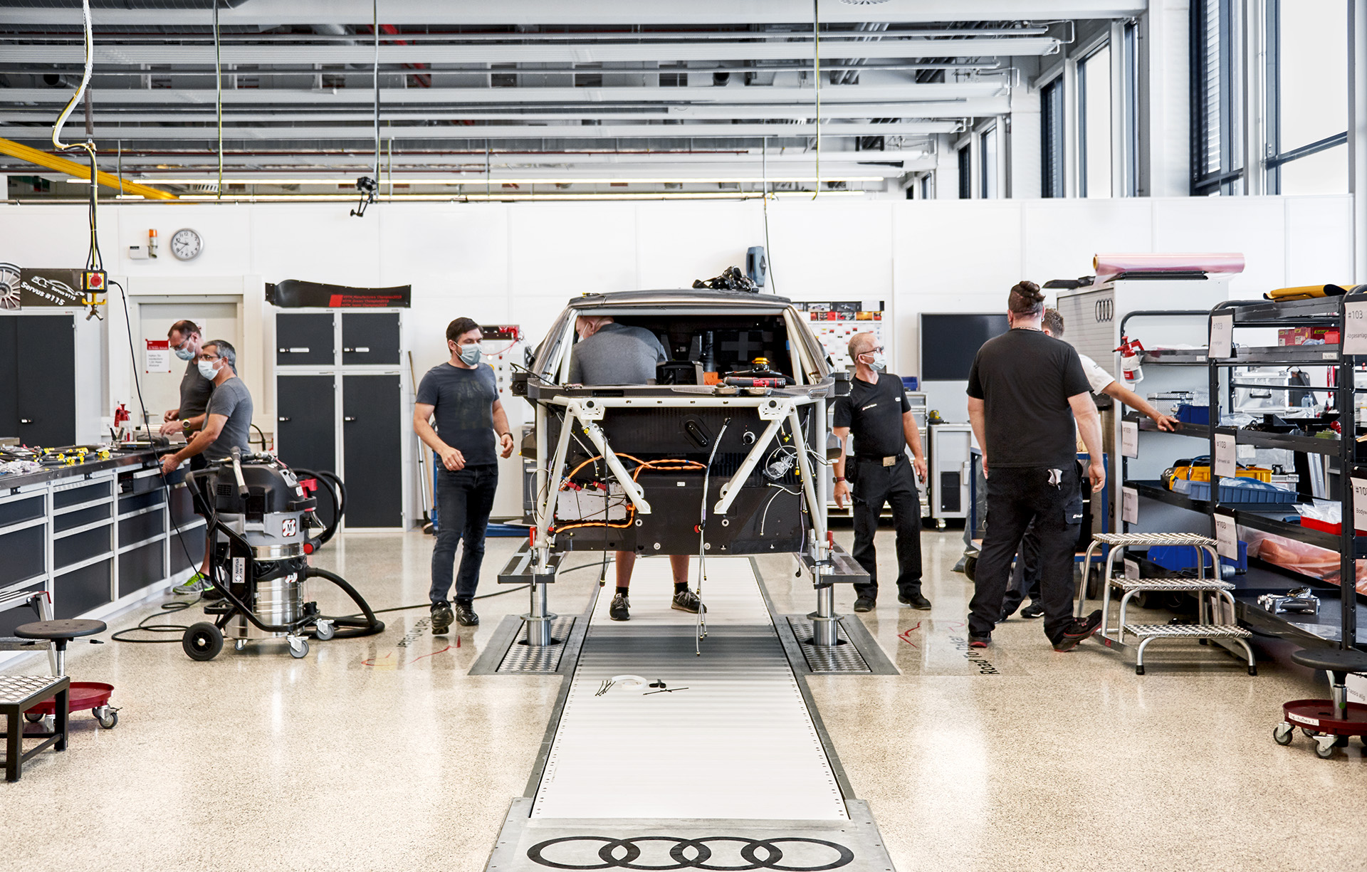  Pracownicy Audi Sport pracują w warsztacie nad podwyższoną klatką samochodu rajdowego.