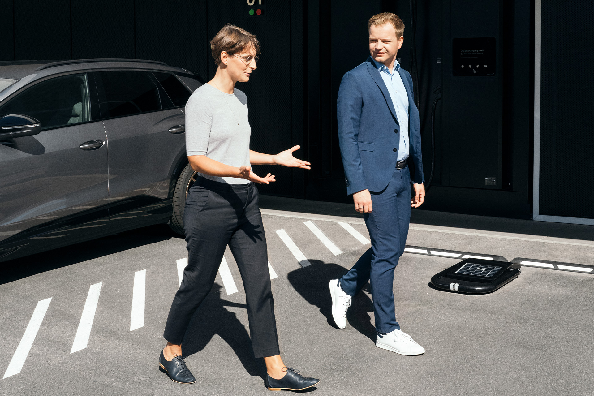 Eksperci ds. zrównoważonego rozwoju dr Johanna Klewitz i Malte Vömel przechodzą przez parking przed hubem ładowania Audi w Norymberdze.