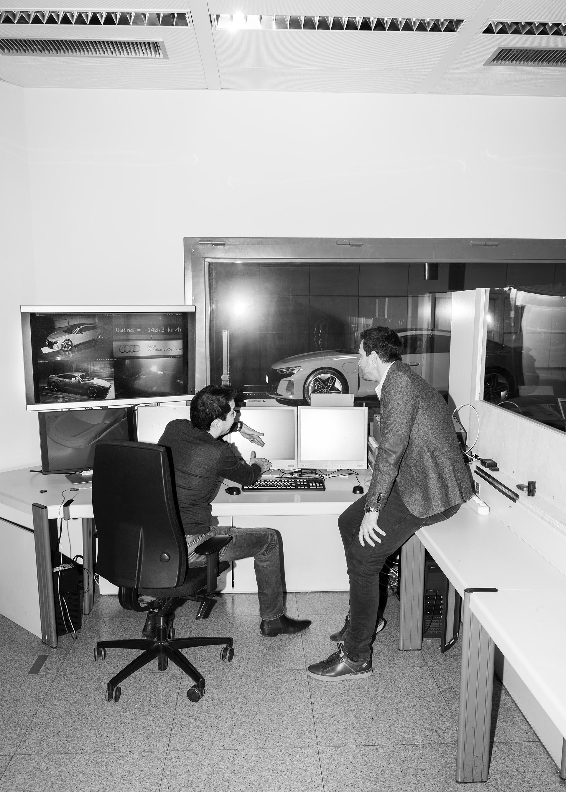 Doktor Kentaro Zens i Thomas Redenbach dyskutują przed wieloma ekranami komputerów, a Audi RS e-tron GT{ft_rs-e-tron-gt} za oknem w tle.