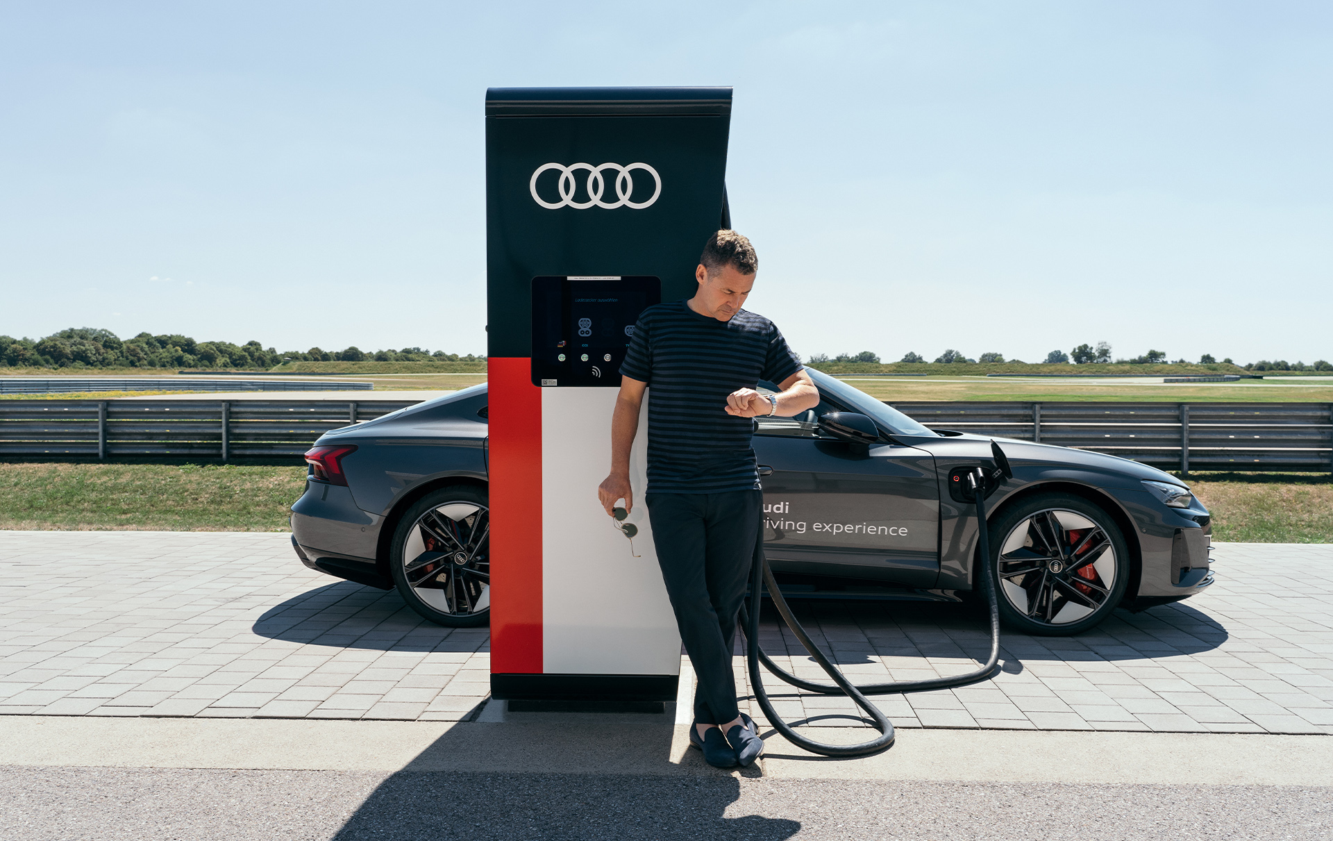 Tom Kristensen opiera się o punkt ładowania podczas ładowania Audi RS e-tron GT.