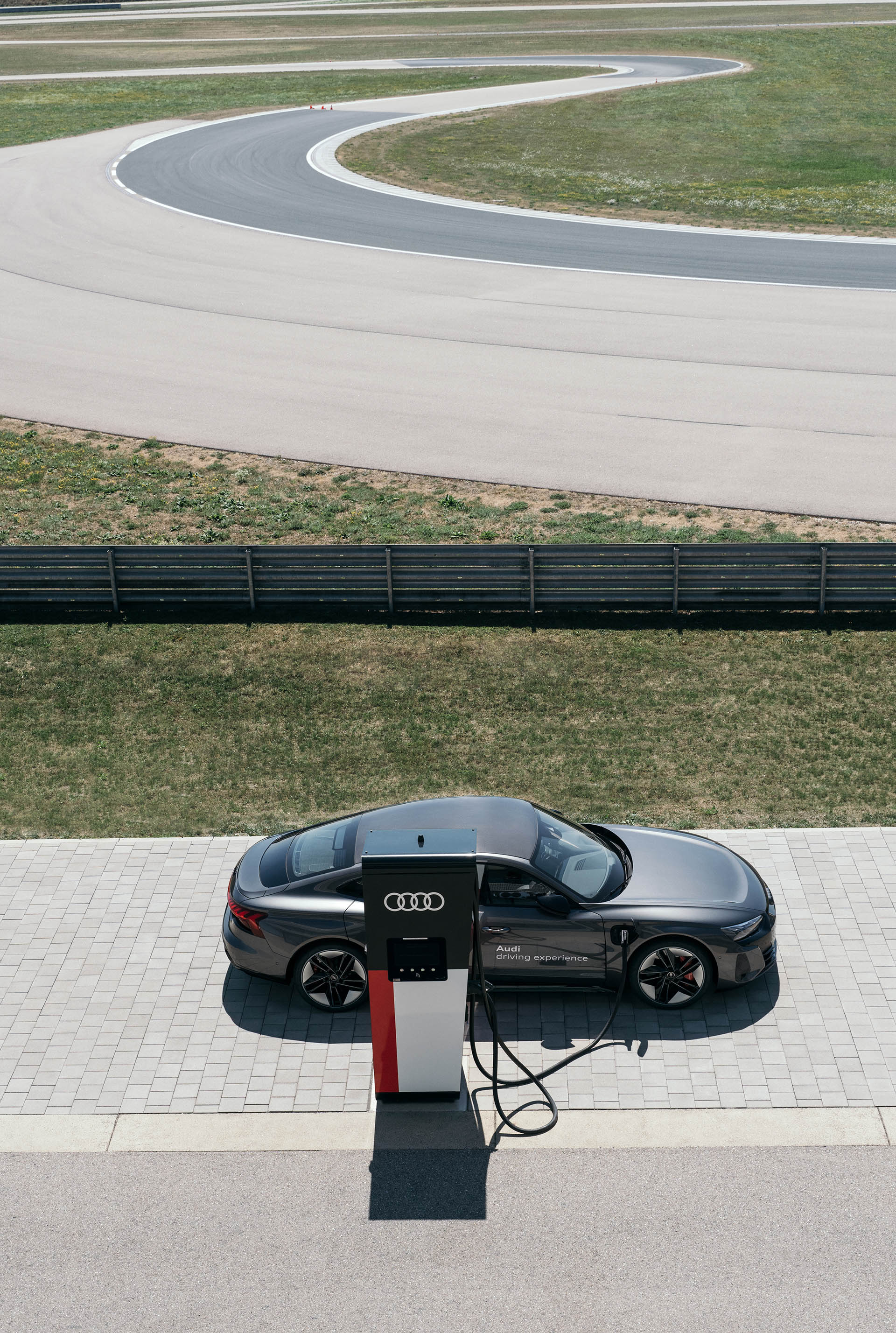 Audi RS e-tron GT ładuje się na pierwszym planie, w tle widać tor wyścigowy.