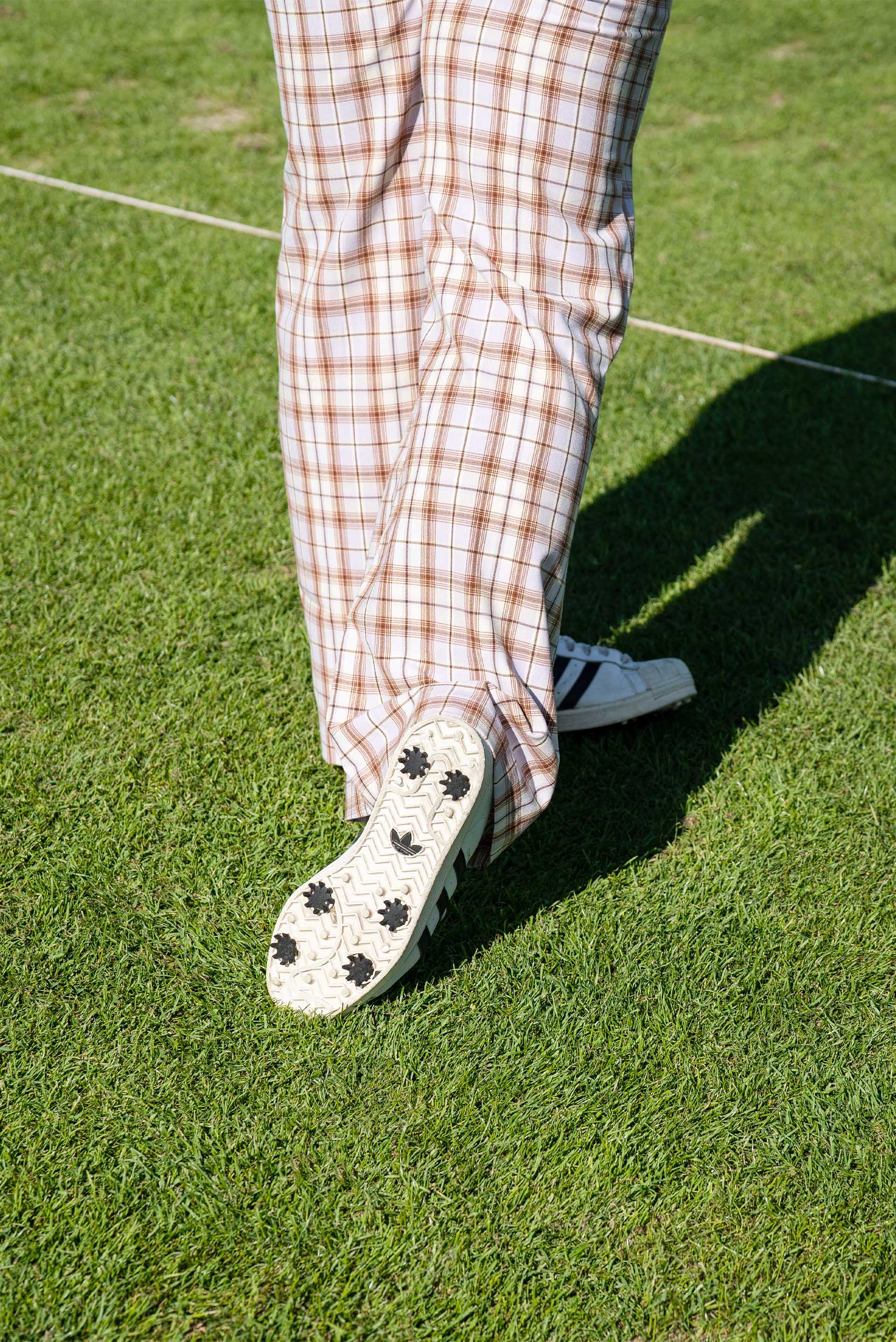 Szczegółowe ujęcie spodni golfowych i tenisówek w kratkę, które Mullins nosi na polu golfowym.