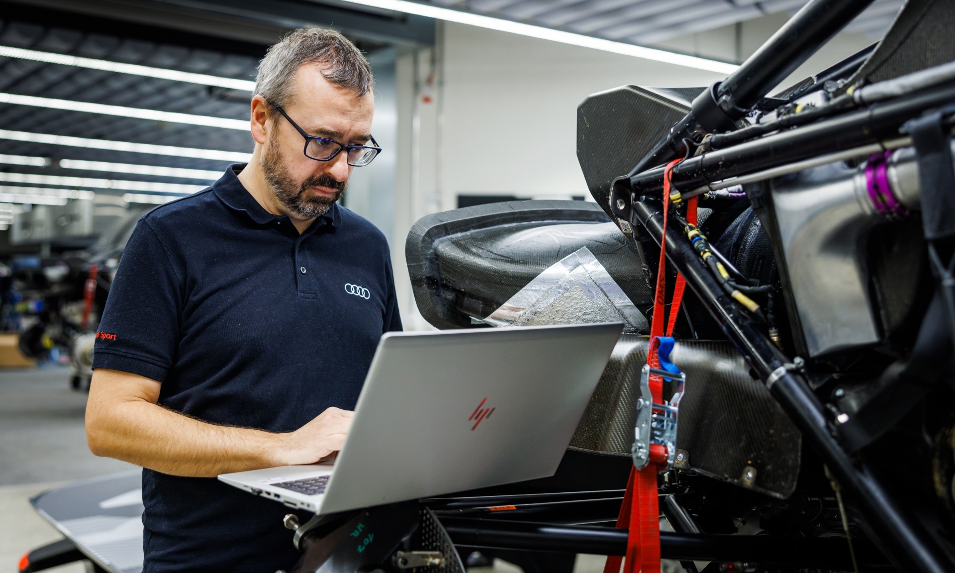 Arnau Nibuó Bosch w sytuacji roboczej przy komputerze obok zdemontowanego Audi RS Q e-tron.