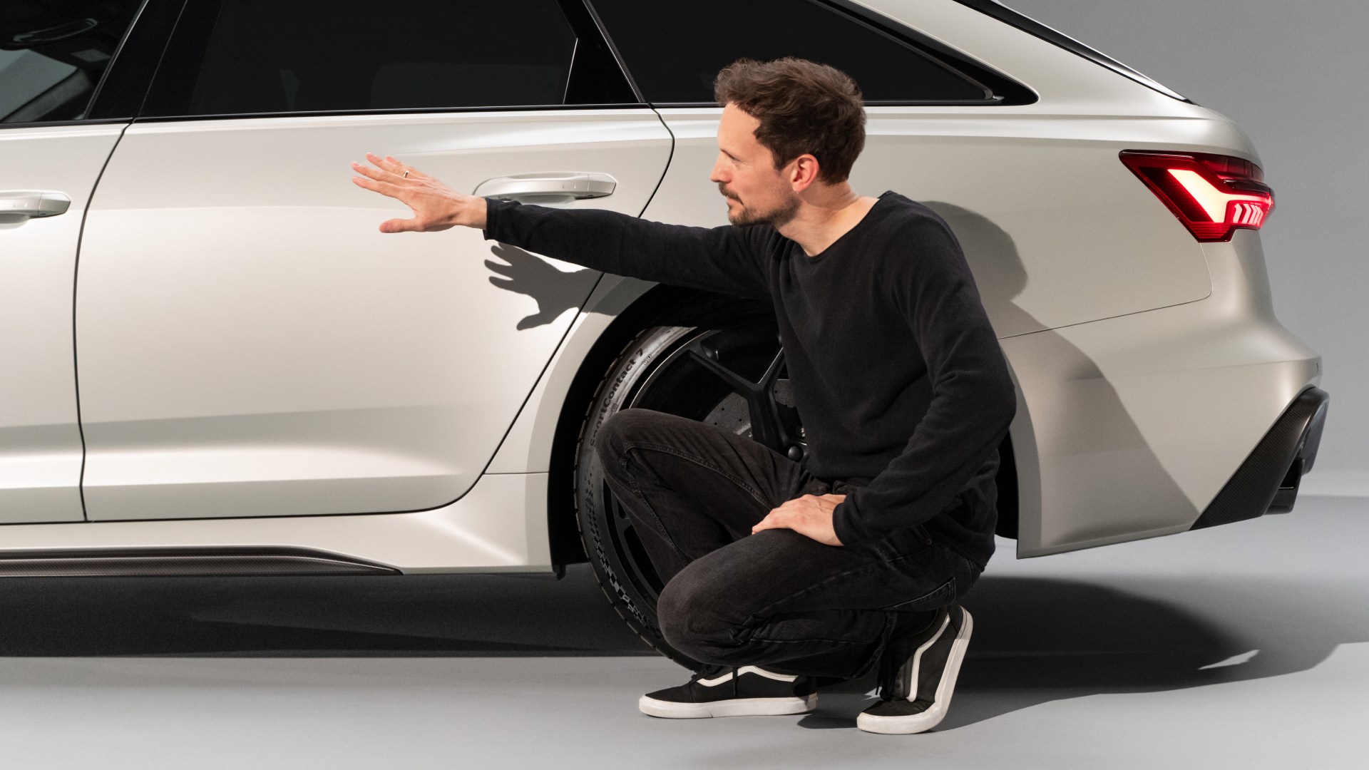 Markus Eberle przykucnął z boku Audi RS 6 Avant, wskazując ręką na tylne drzwi.